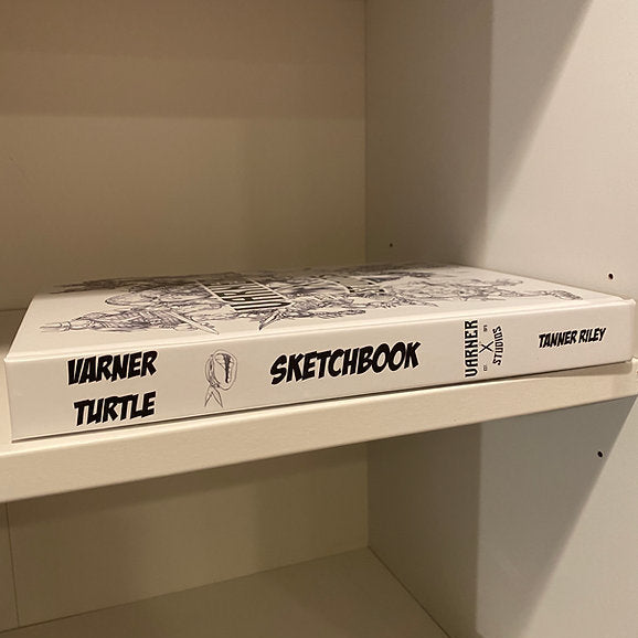 A hardcover sketchbook titled 'Warner Turtle Sketchbook' resting on a white shelf inside a white wooden cabinet or shelf unit.